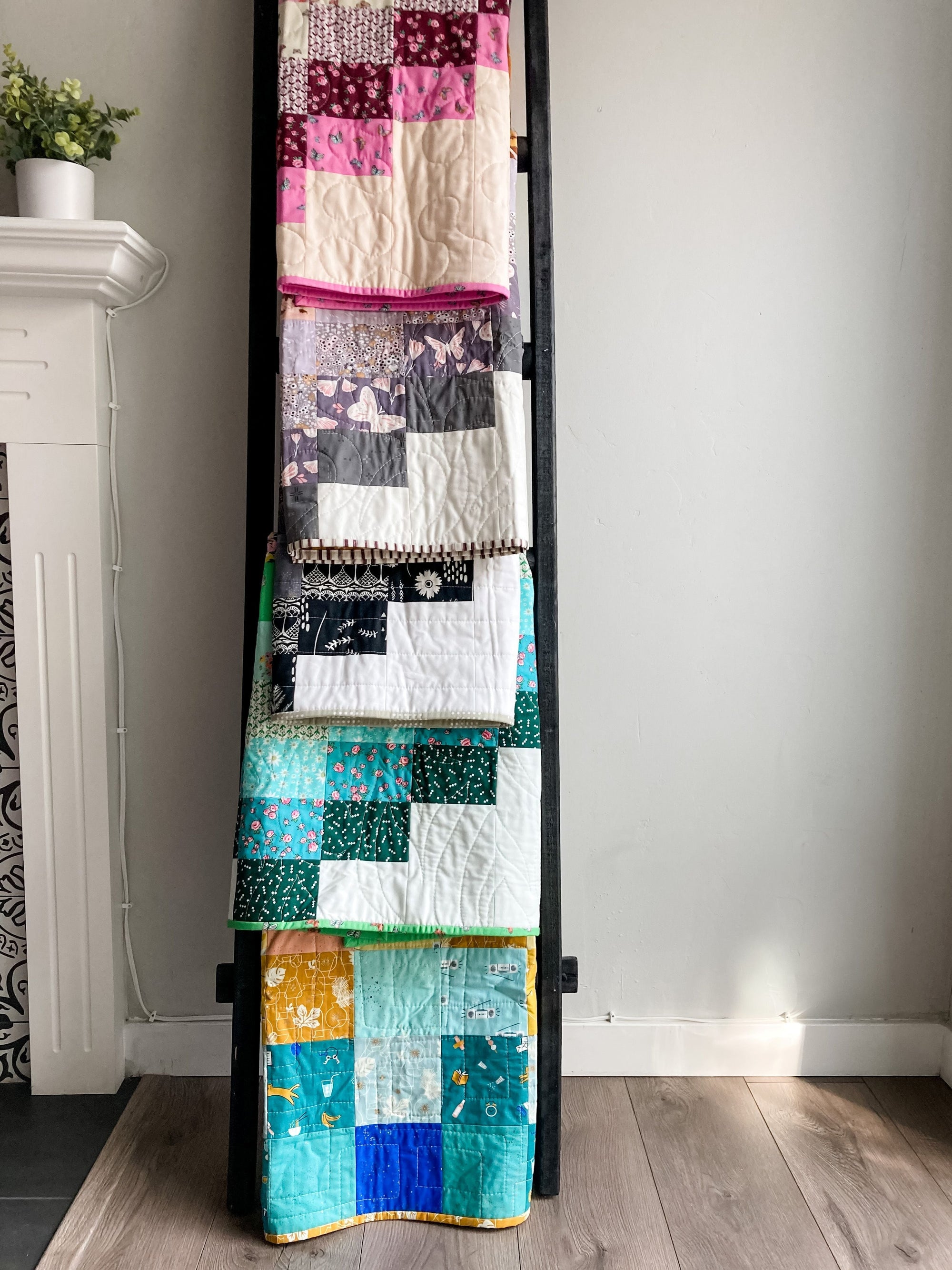 five colorful patchwork baby quilts on a quilt ladder
