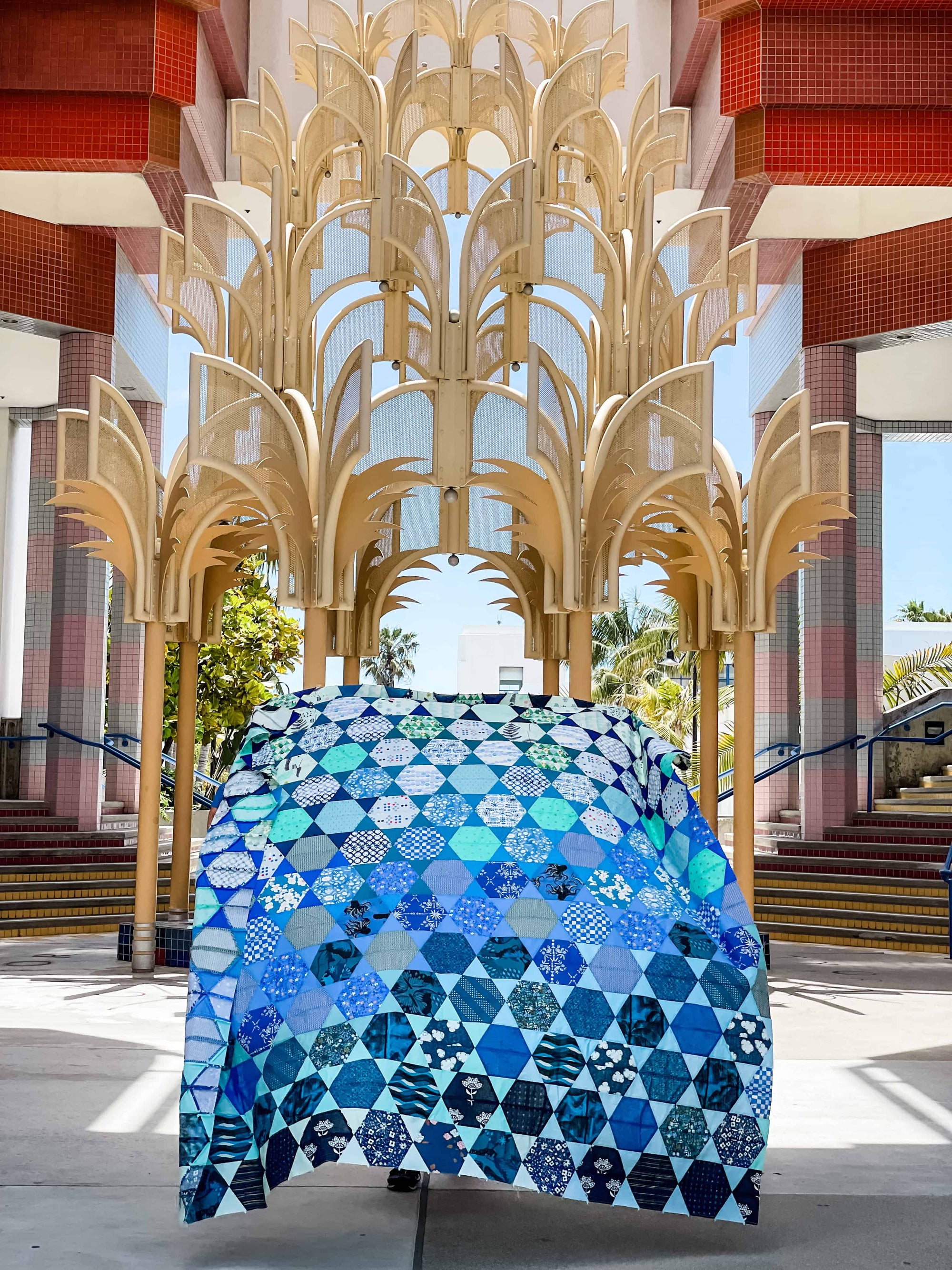 A blue gradient patchwork quilt held up in front of large, gold architectural arch