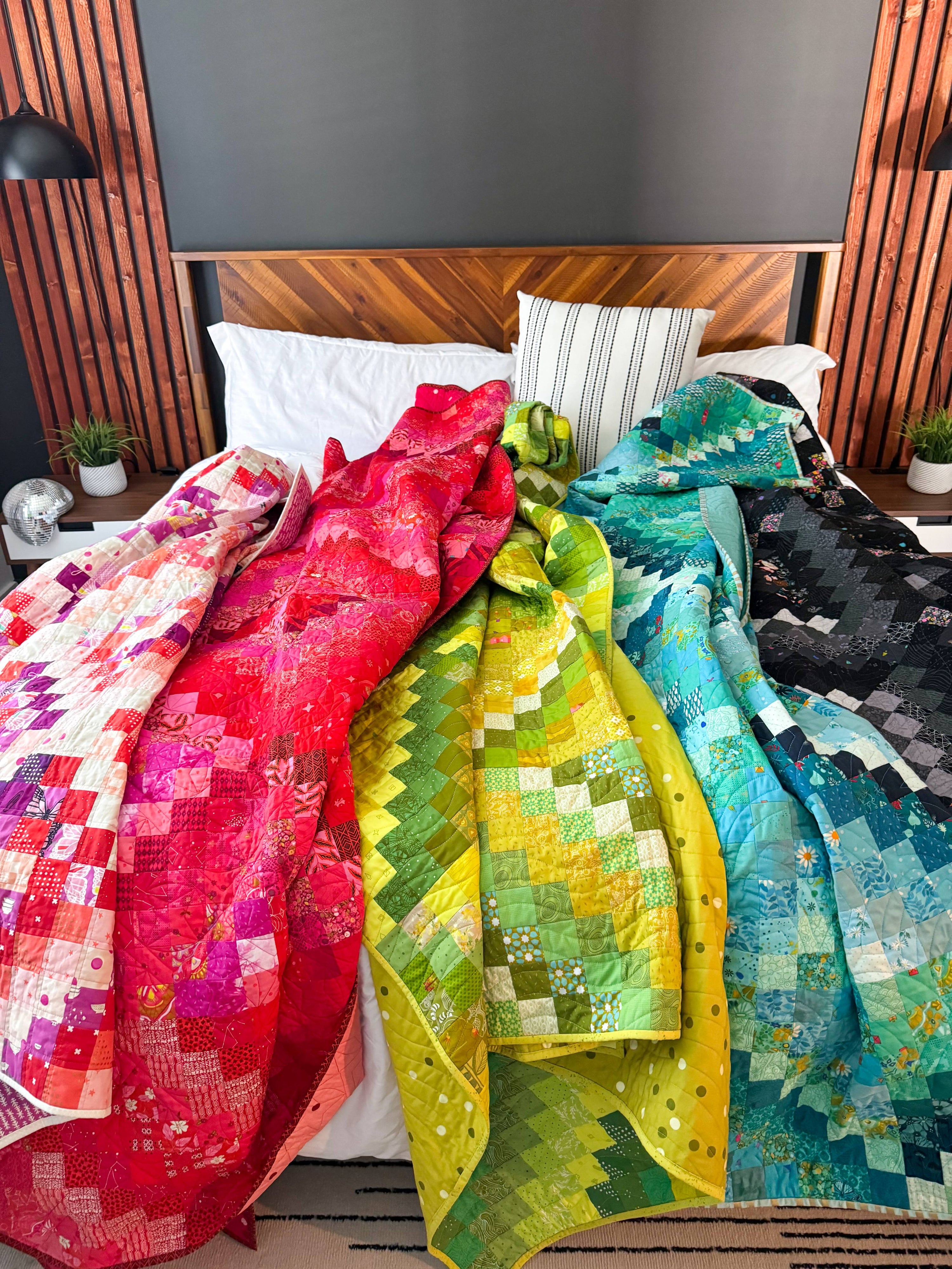 5 colorful patchwork quilts strewn on a bed