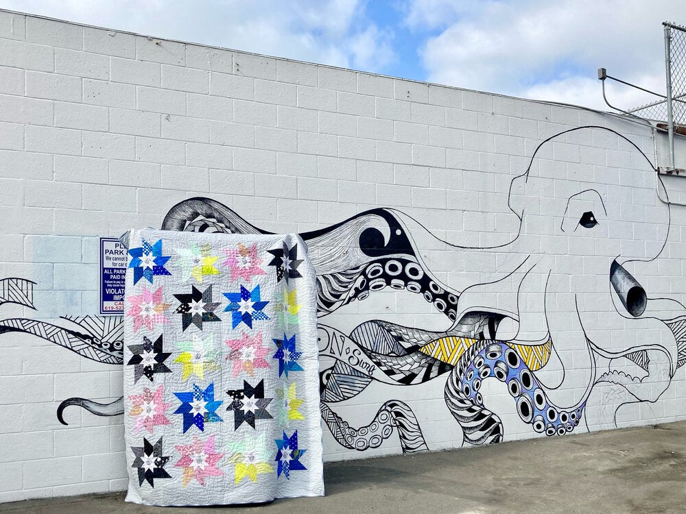 patchwork quilt with eight point star blocks, in front of large octopus mural