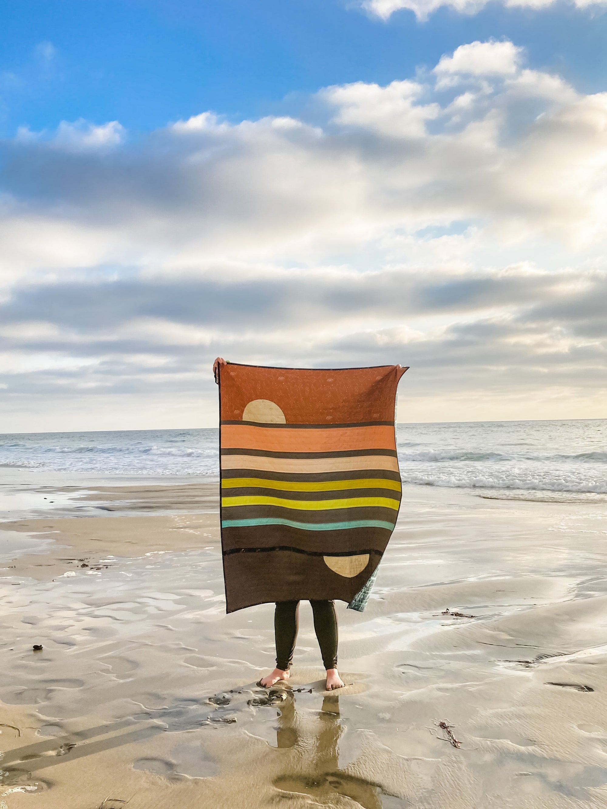patchwork quilt with mid-mod design in retro sunset colors, on a beach at sunset