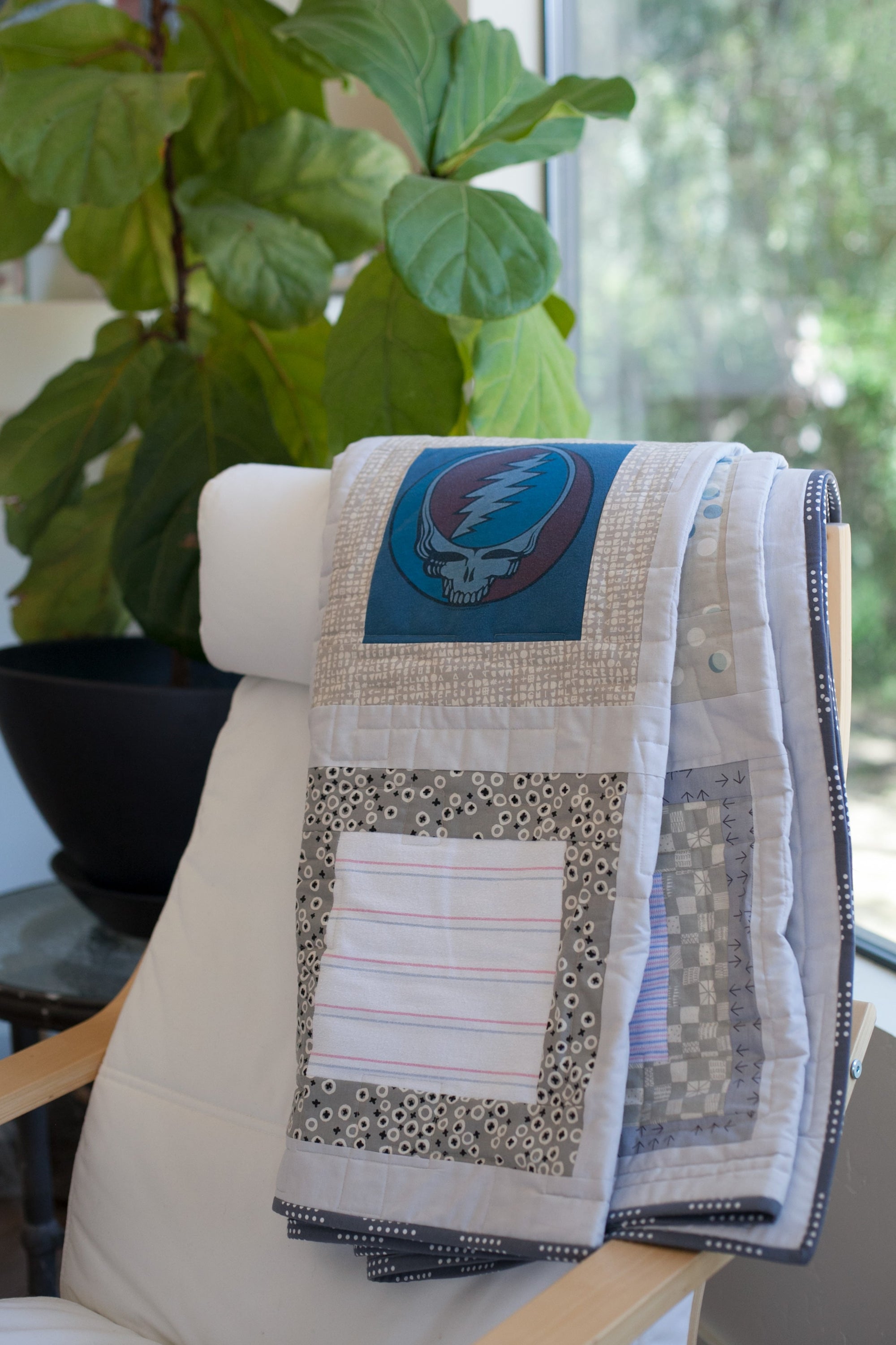 gray upcycled baby clothes quilt, folded and draped over chair in modern space