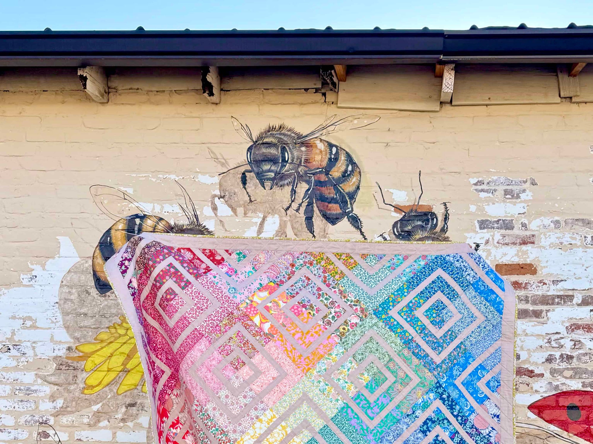rainbow gradient quilt with liberty of london fabrics in front of a mural with bees and other pollinators