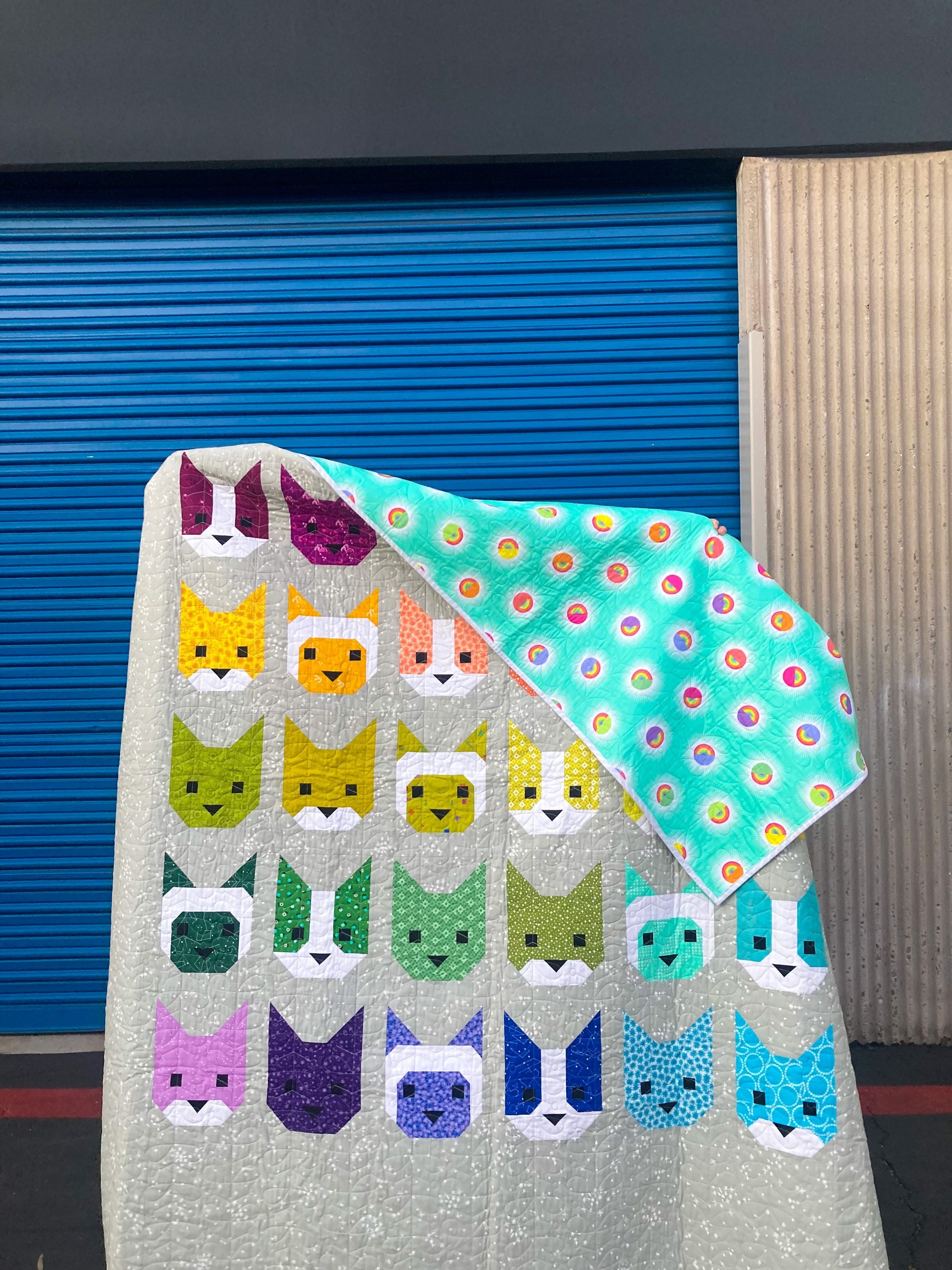 rainbow kitties patchwork quilt held up so that part of aqua backing shows