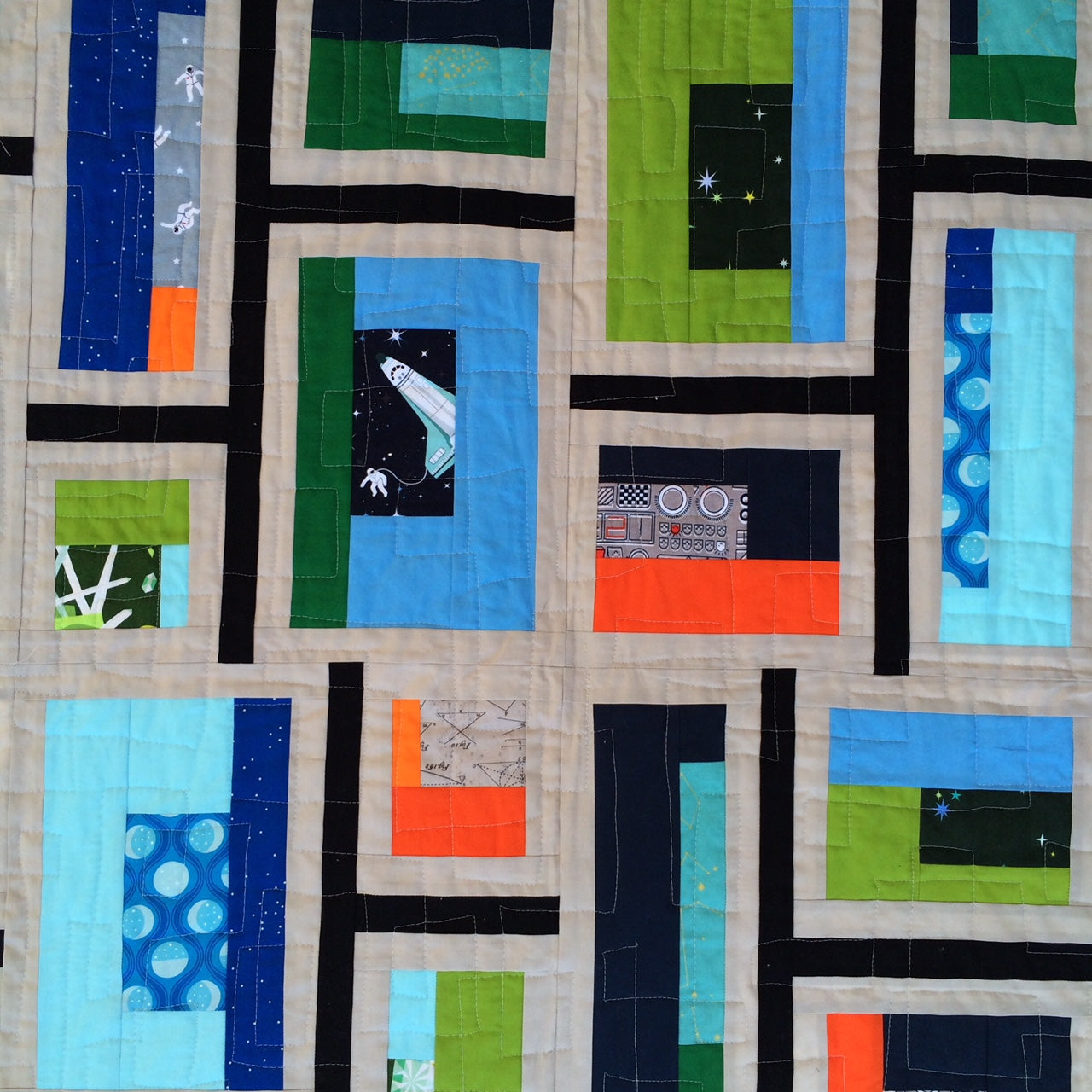 close up on patchwork from a space themed mid-mod quilt with blue, green and orange fabrics