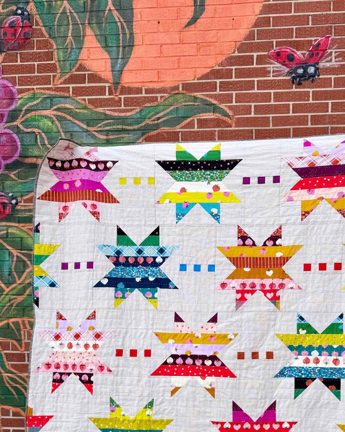 patchwork star quilt with brightly colored strawberry fabric in front of a brick mural