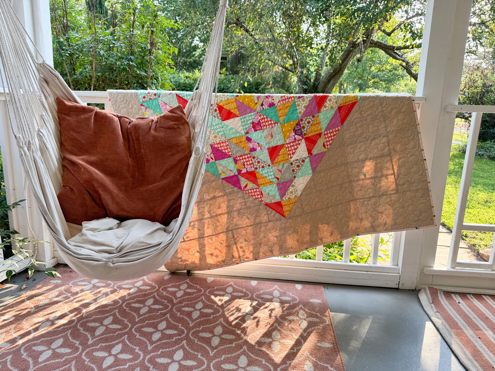 Hanging chair with a colorful quilt draped over it on a porch.