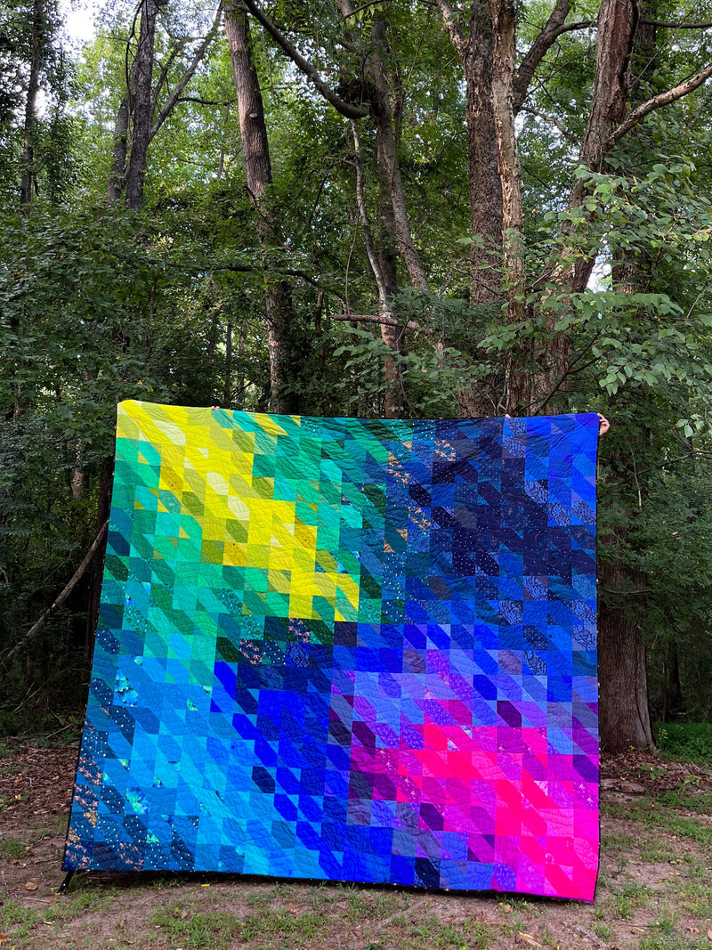 Colorful quilt with a pixelated pattern in a forest setting