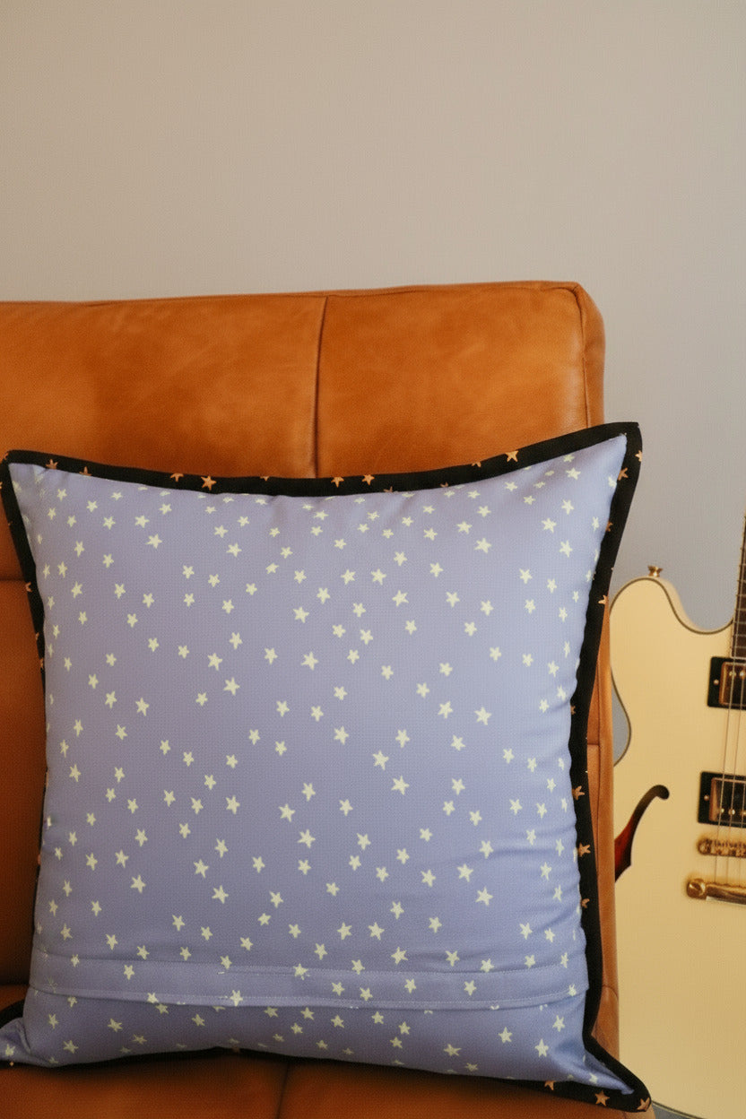 Brown leather chair with a blue pillow featuring star patterns in front of a guitar and wall background