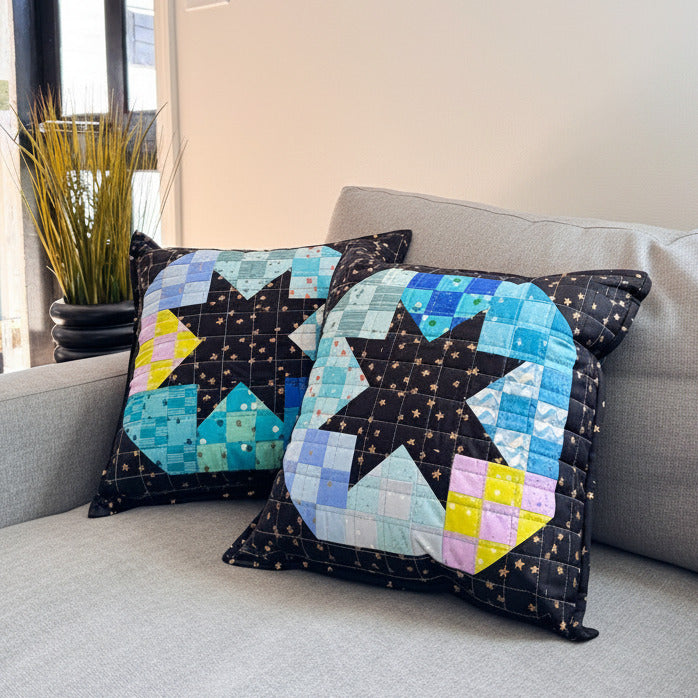 quilted disco ball star pillows in cool colors on neutral gray couch with plant behind them. 