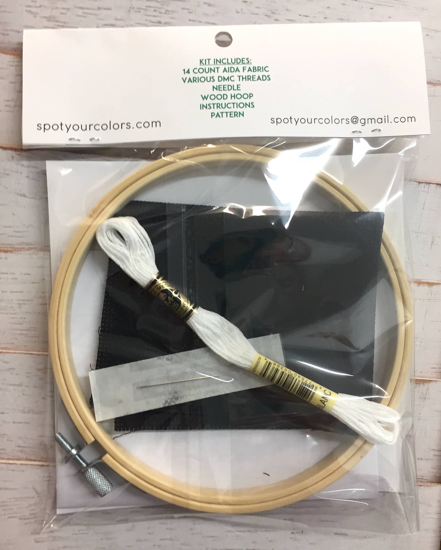 Embroidery hoop kit with thread and accessories in clear packaging on a wooden surface.