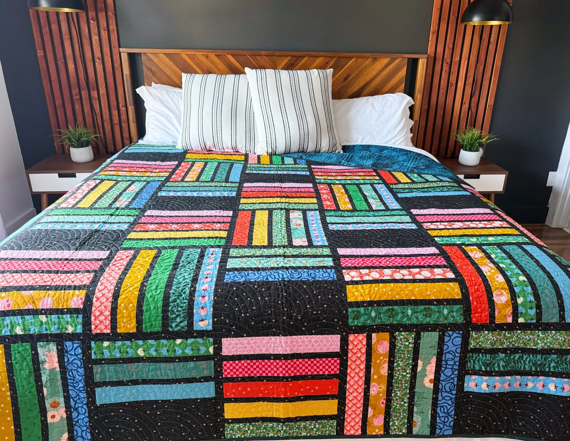 Colorful modern rainbow quilt on a bed with a wooden headboard and side tables.