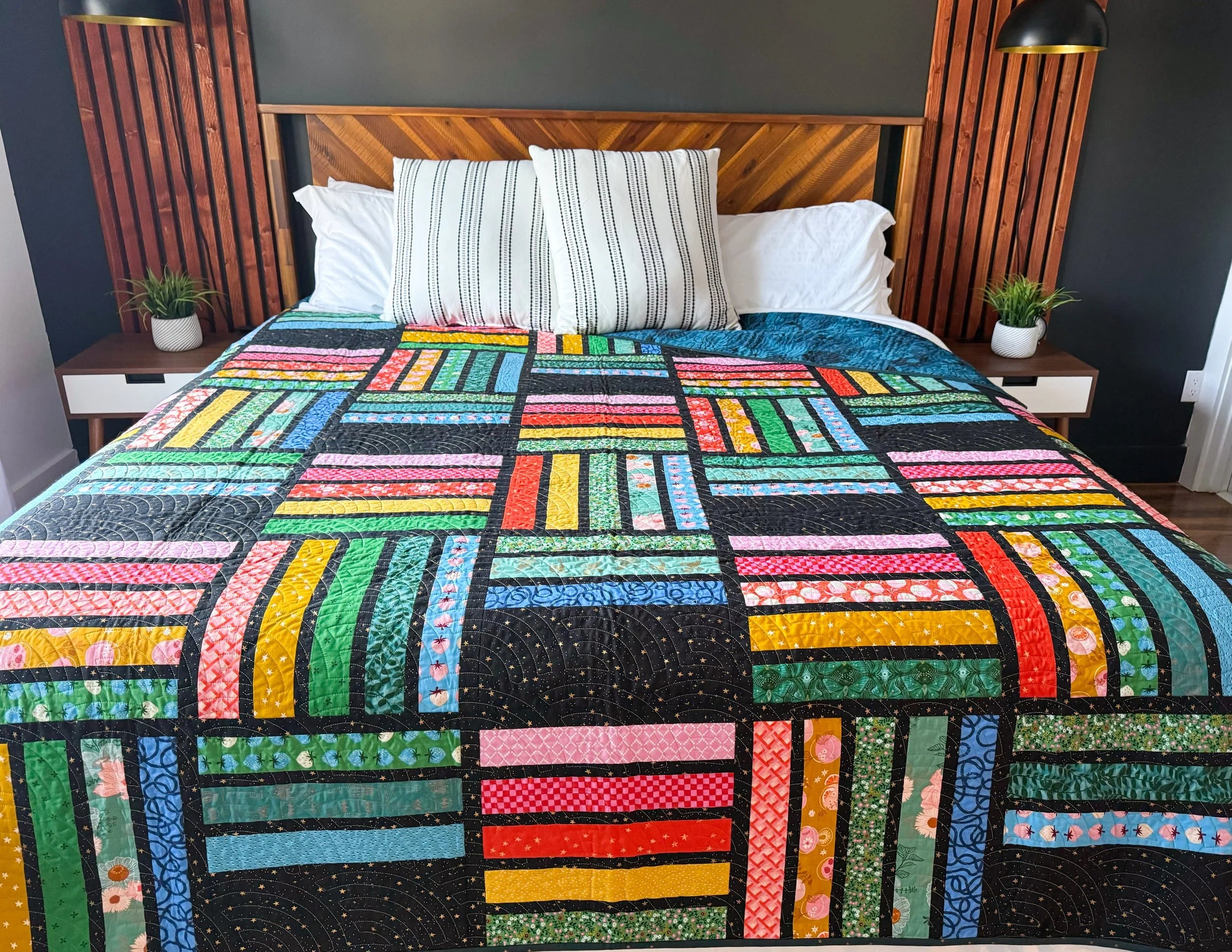 Colorful modern rainbow quilt on a bed with a wooden headboard and side tables.
